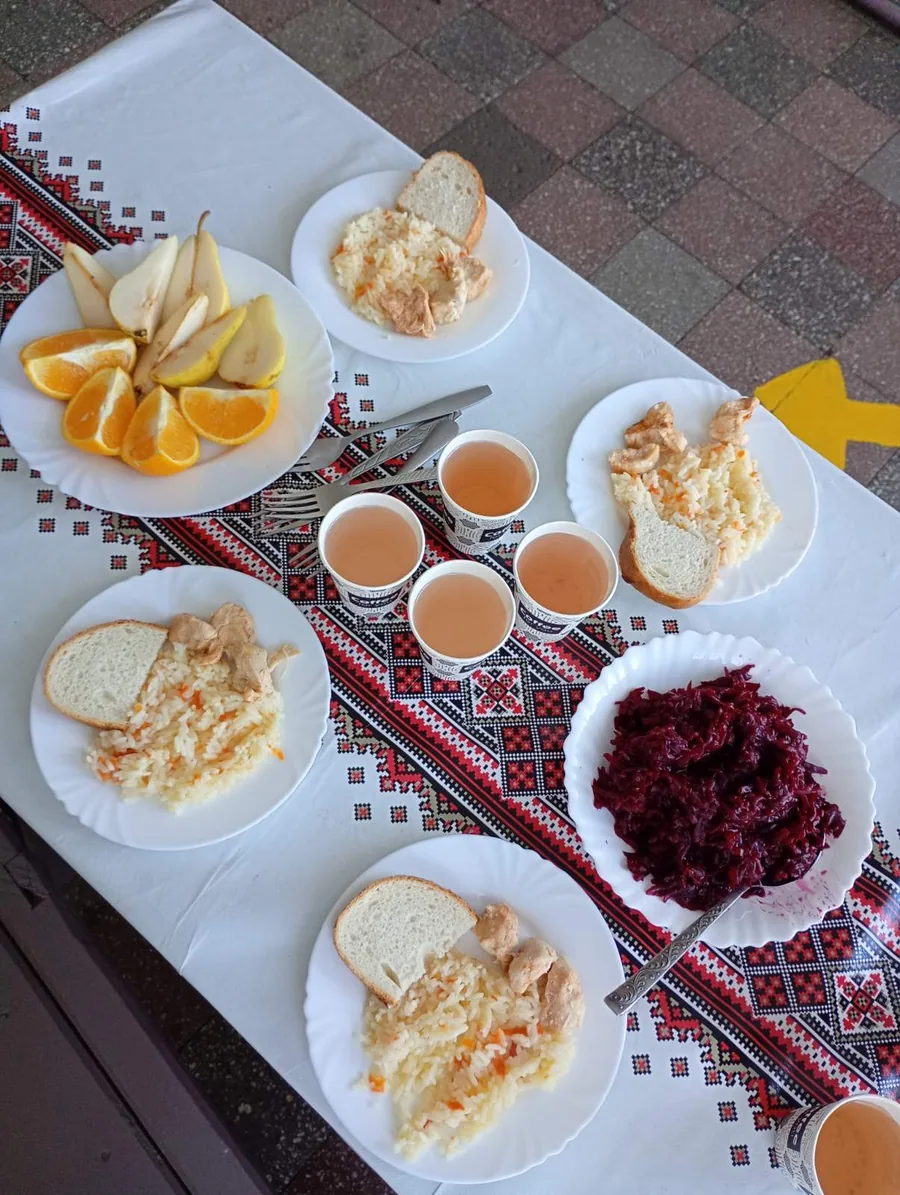 Порції рису з куркою та хлібом, салат із буряка, фрукти й напої на столі